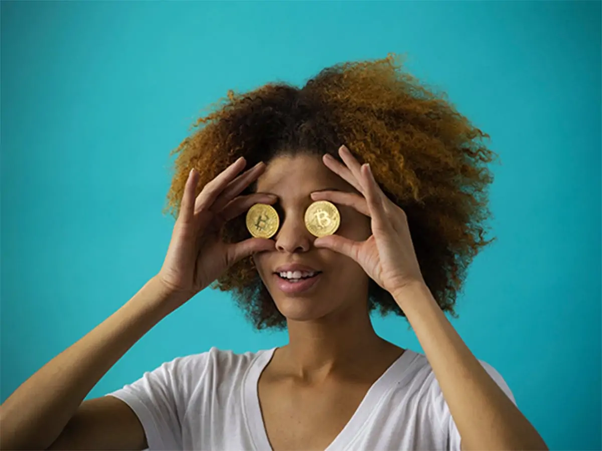 A photo of a woman holding up gold coins up to her eyes.